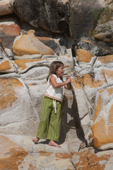 Child wearing a white knit vest with red candy canes and green towelling pants standing on a stone surface.
