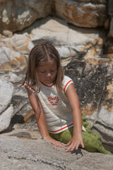 Child wearing a white knit vest with red candy canes and green towelling pants standing on a stone surface.