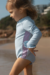 Child wearing a light blue and purple swimsuit on a beach