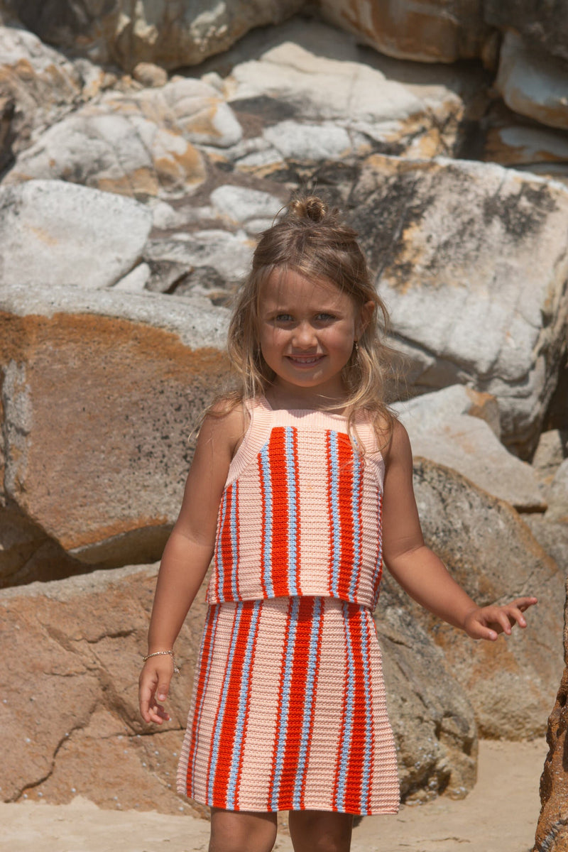Young girl in a striped top and skirt standing among rocks