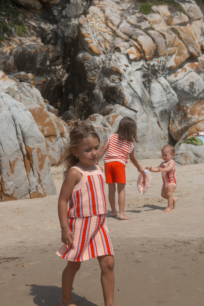 Children in matching red and white outfits playing on a rocky beach.