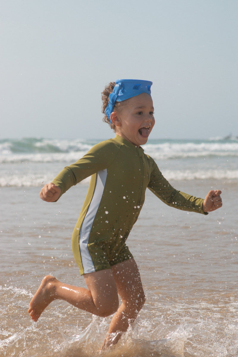 Child running on a beach wearing a green swimsuit and blue snorkle.